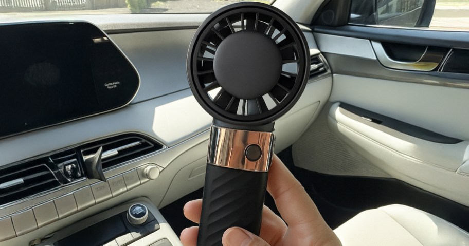 person holding black personal fan in their car